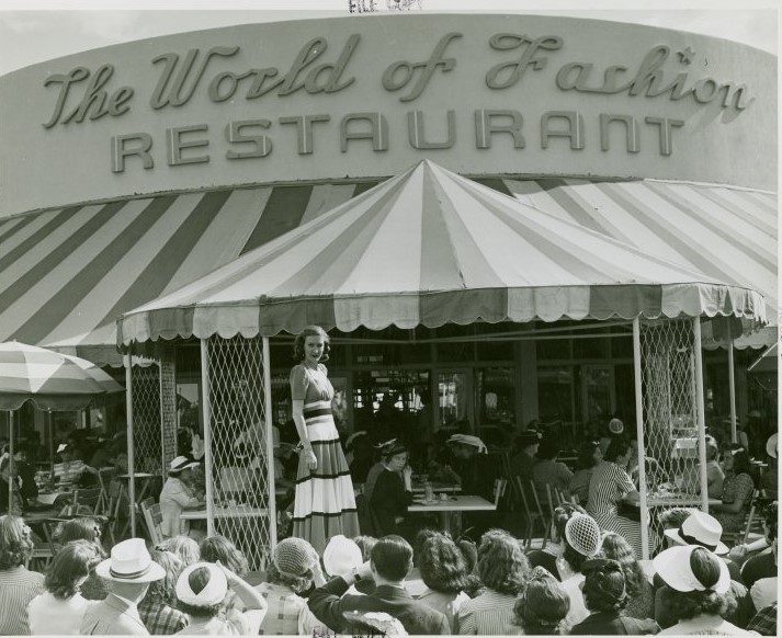 1930s vintage photo of the World of Fashion Restaurant at the 1939/1940 New York World's Fair. The image features a fashion show happening out front.