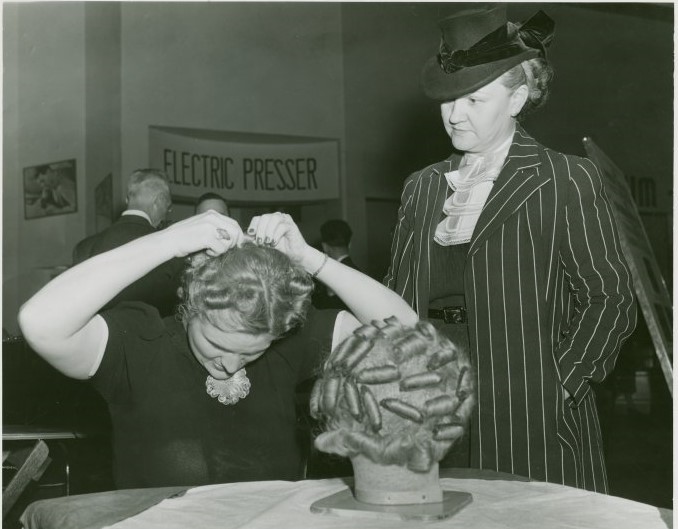 1940s vintage photo: A woman in 1940 at the New York World's Fair at the 'World of Fashion' Exhibit practicing how to set her hair in curlers for an early 1940 hairstyle. 