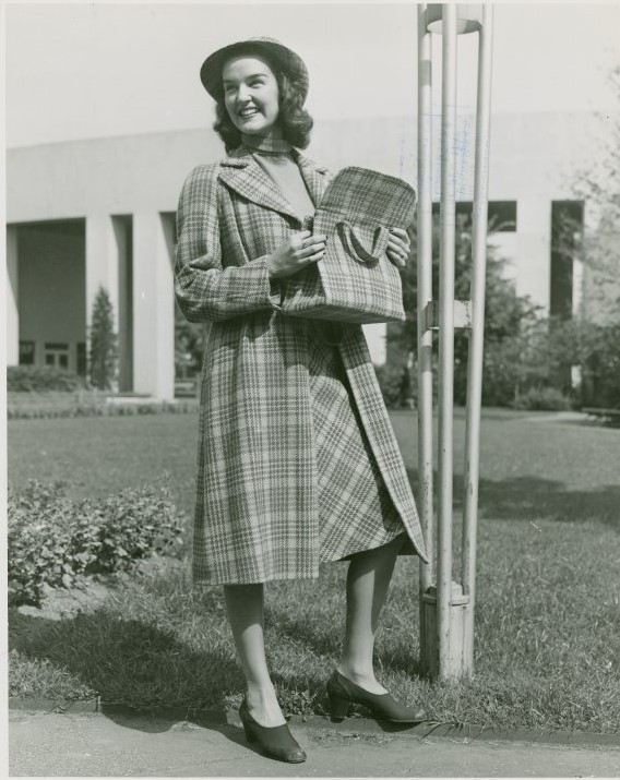 1940s fashion as seen in a 1940 vintage photo from the World of Fashion at the 1940 New York City World's Fair. The woman is wearing a long plaid jacket, matching skirt and plaid purse. 