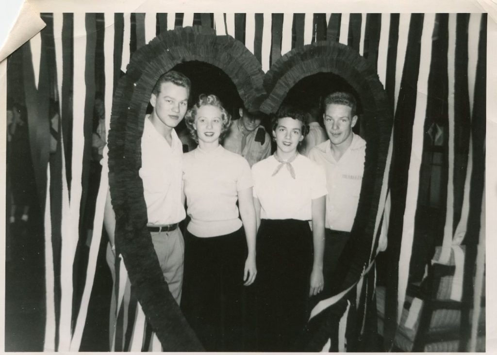 1950s vintage photo of a Valentines Day Dance decoration of a giant heart with streamers and 1950s couples posing in the heart