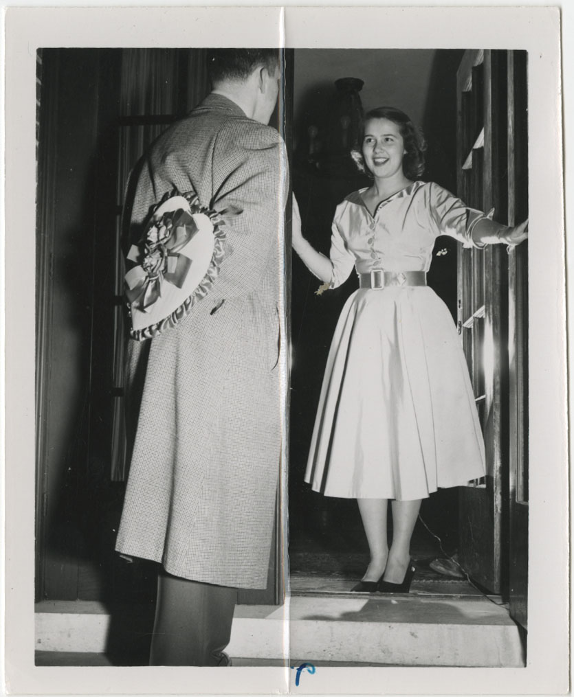 1950s vintage photo of a young woman university student in a 1950s dress receiving a box of heart chocolates on Valentines Day at the door from her date.