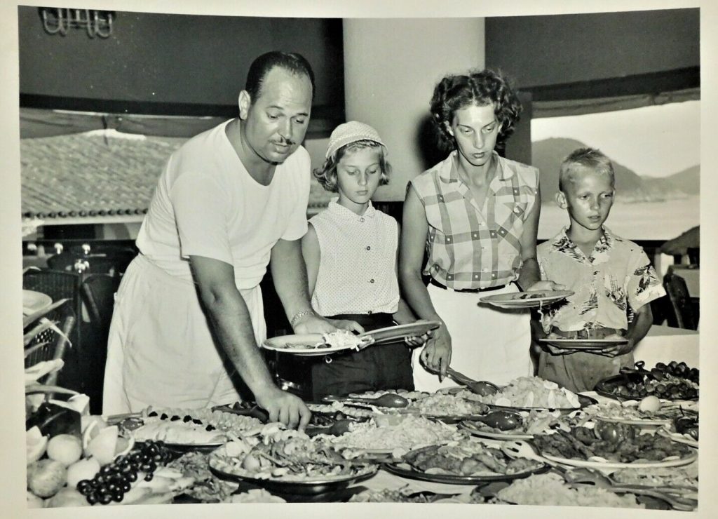 1950s vintage photo of a family on vacation eating at the buffet in 1950s fashions. Fun vintage vacation photo