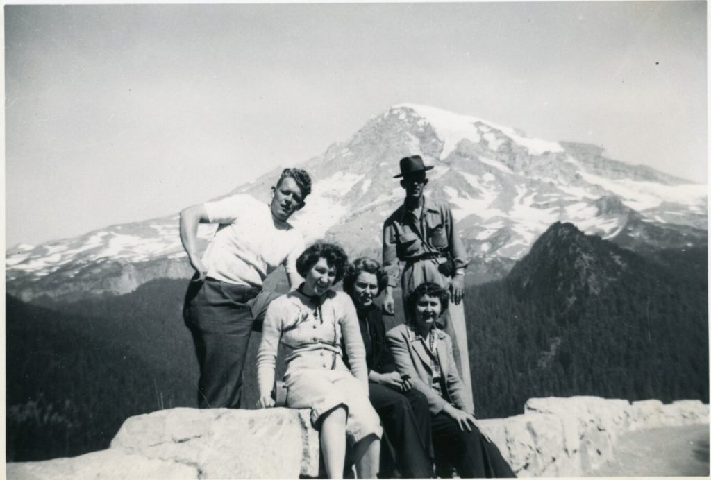 1950s vintage vacation photo of a group of people posing in front of a large mountain covered in snow. 