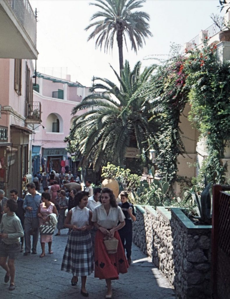 1950s vintage vacation photo of a street seen in 1958 of Capri Italy featuring people walking around in 1950s fashions. 