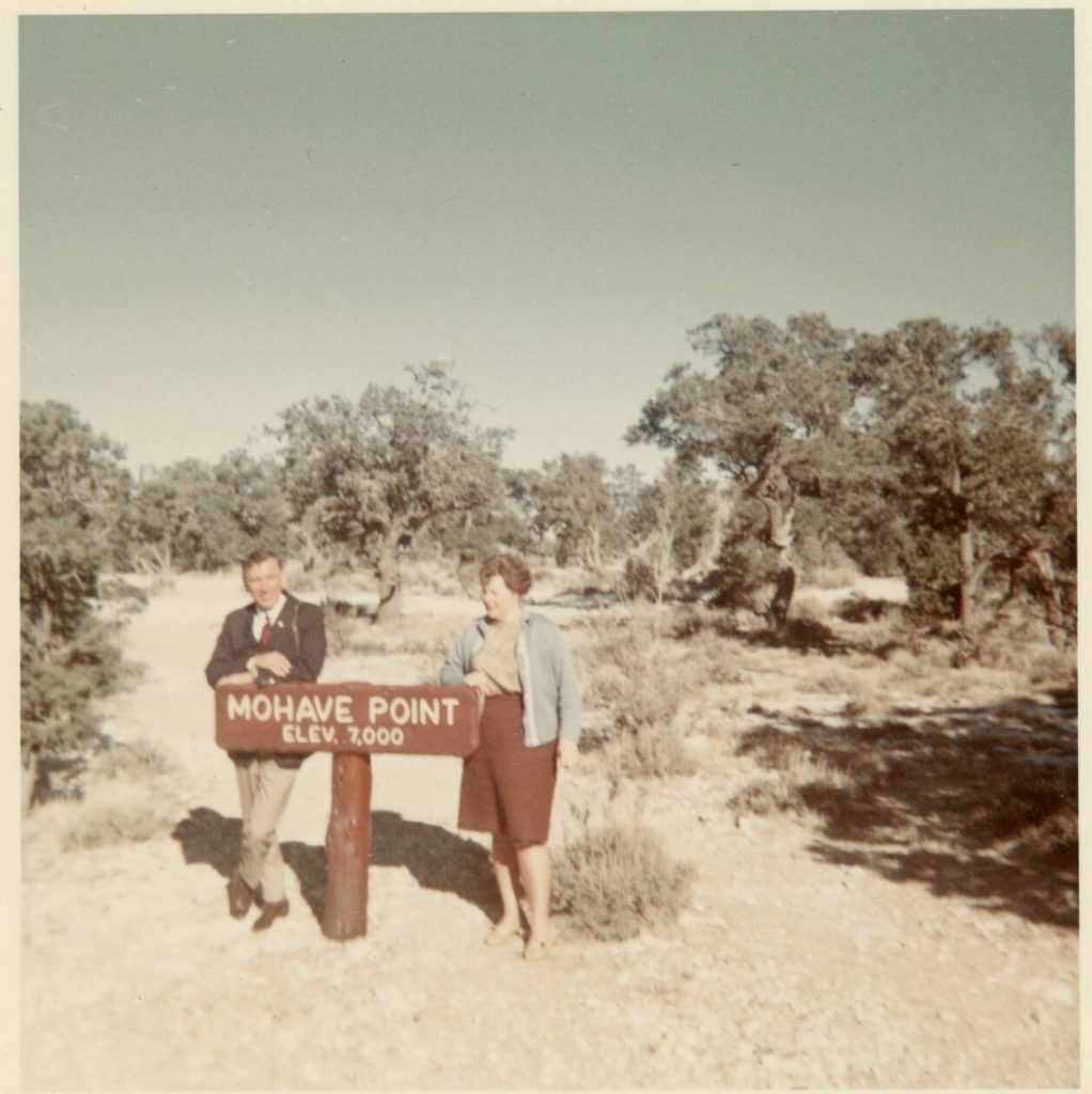 1960s vintage photo of a couple on vacation and posing at the Mohave point sign in 1960s fashions. -Vintage Vacation photo-