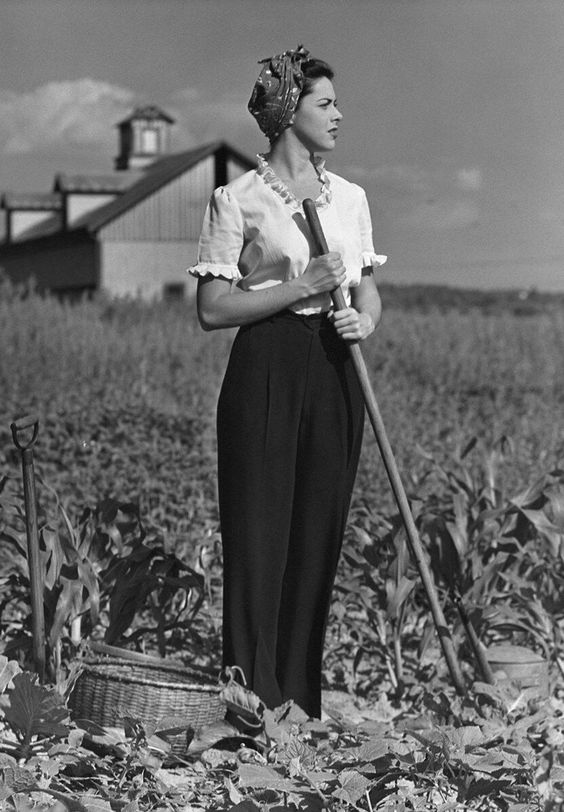 1940s vintage photo of a woman in trousers, hair scarf and blouse working in a garden during WW2. 1940s Fashion Inspiration. 