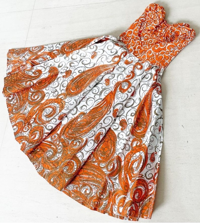 1950s fashion: a 1950s sundress, strapless by Fred Perlberg featuring orange swirls on the fabric and a full circle skirt. 