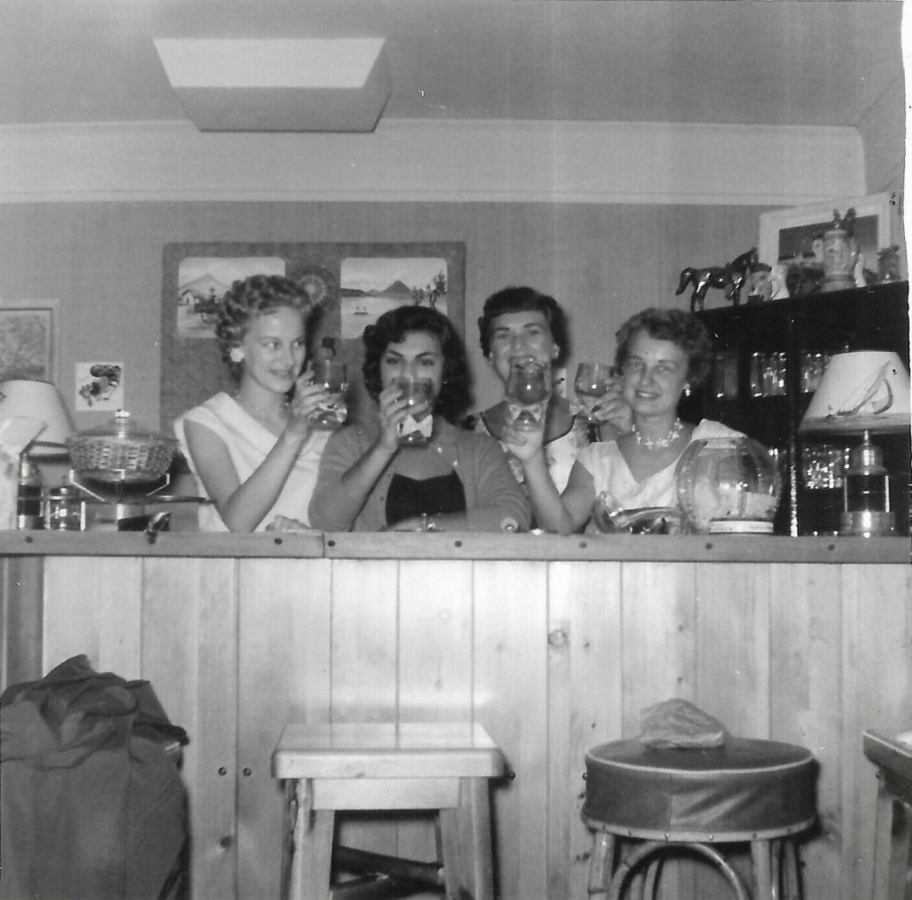 1950s vintage photo of a 1950s bridal shower from 1955 featuring the bride to be and her guests posing with drinks at a home bar.