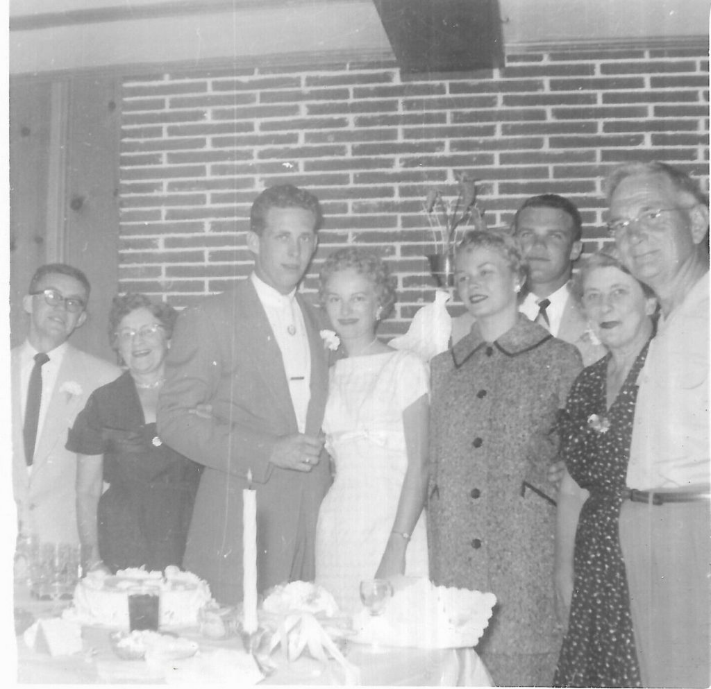 1950s vintage photo of a 1950s wedding featuring the bride in a pencil dress as her 1950s wedding dress posing with family