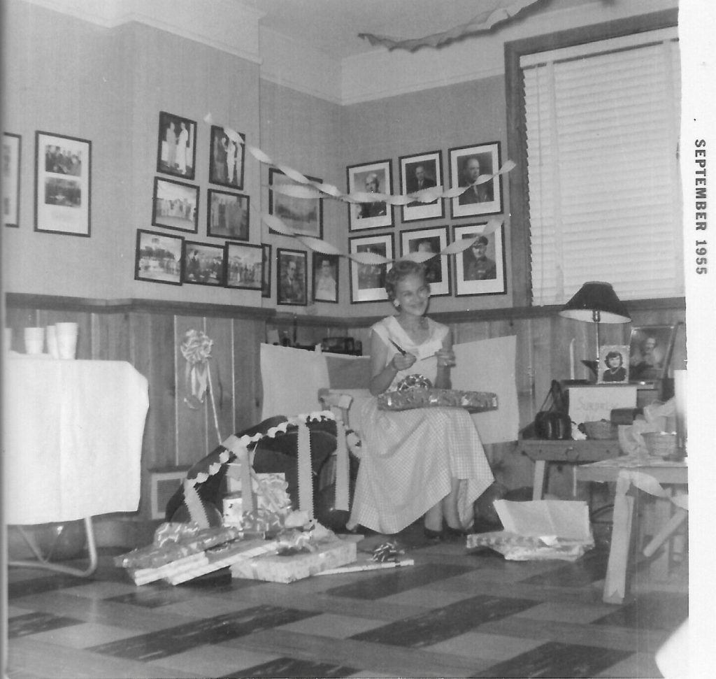 1950s vintage photo of a bridal shower from 1955 featuring the bride to be opening gifts with decorations all around her in a 1950s dress.