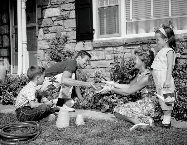 1960s vintage photo of a family working in their garden in front of their house in 1960s summer fashions for kids and adults. 