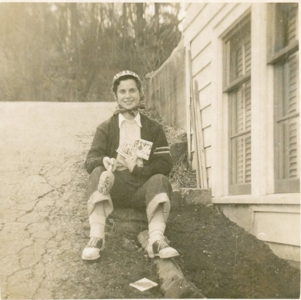 1940s (maybe 1950s) photo of a woman in saddle shoes holding seed packets & a garden trowel ready to plant.