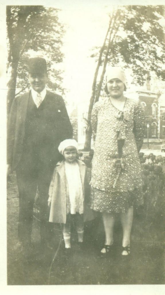 1920s vintage photo of a 1920s family posing together. The 1920s mother is a 1920s maternity wear dress posing with her young daughter and husband outside. Fantastic 1920s shoes on the woman. 