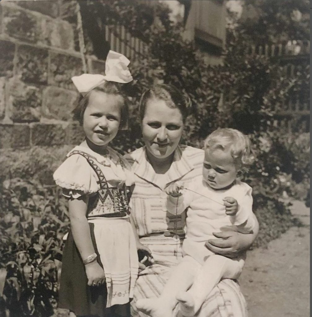 1930s vintage photo of a mother posing with her young kids. The daughter is wearing a dirndl and big bow in her hair