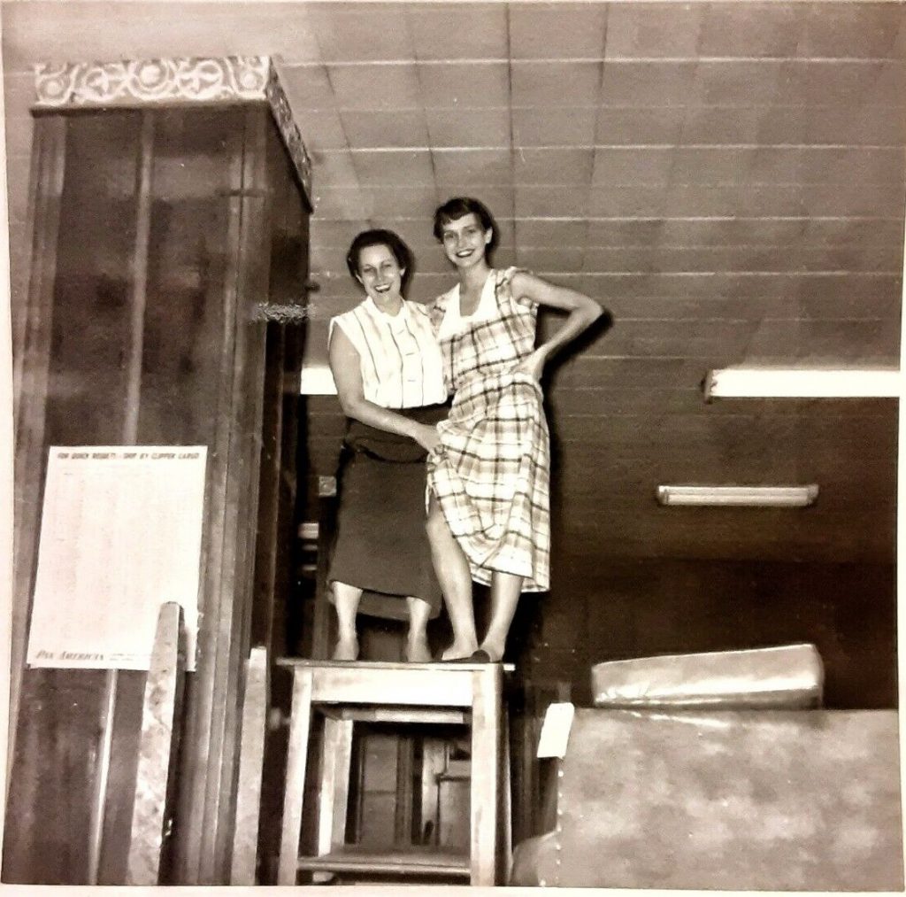 1950s vintage photo of a mother holding up the hem of her daughters plaid dress while standing on a table. Optical Illusion photo