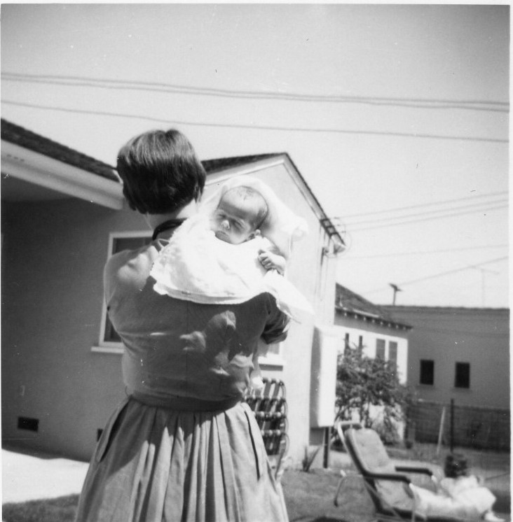 1950s vintage photo from 1958 of a young mother holding her new baby in the front yard. 