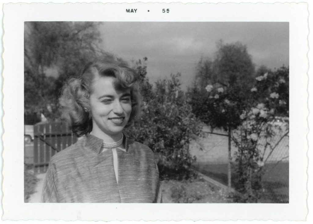 1950s vintage photo of a young woman with a 1950s hairstyles and pearl necklace smiling at the camera. Super 1950s vintage hairstyle inspiration