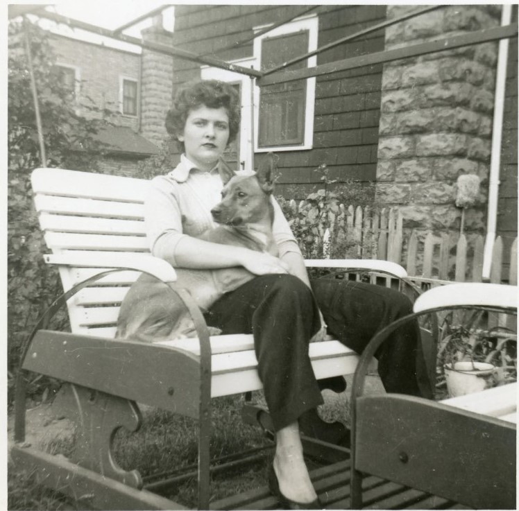 1950s vintage photo of a young woman with a 1950s hairstyle holding a dog on her porch swing. 