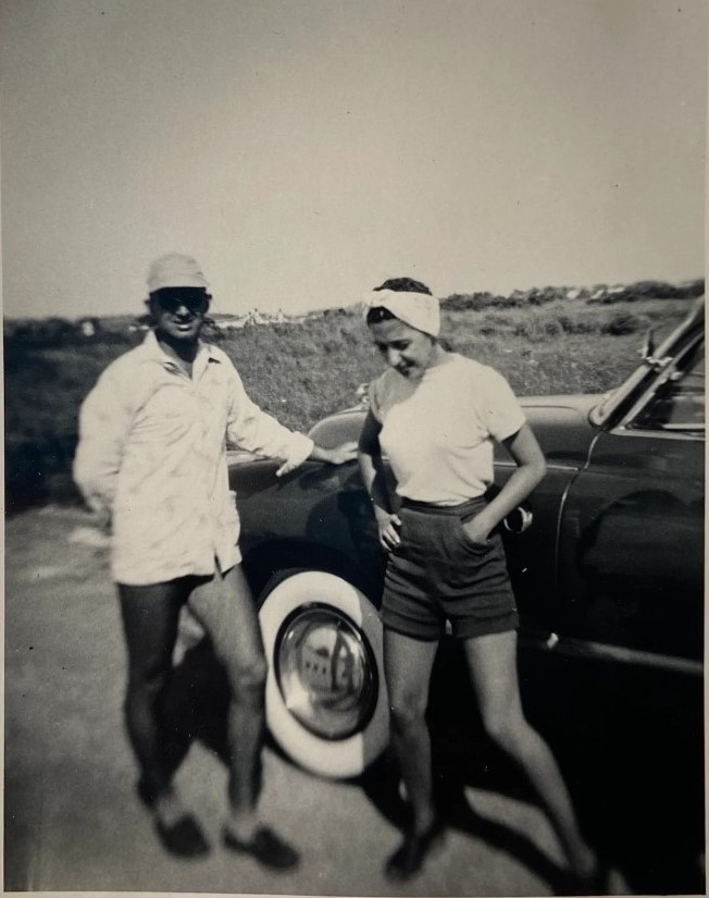 1940s maybe 1950s vintage photo of a man and woman in shorts posing by their car during the summer time. 