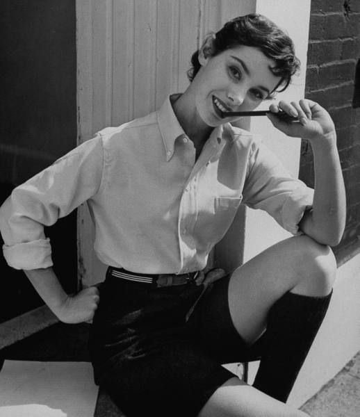 1950s photo from 1954 of a woman wearing a Classic campus outfit of men's clothes including pink shirt, bermuda shorts, and striped elastic belt, all from Brooks Brothers.