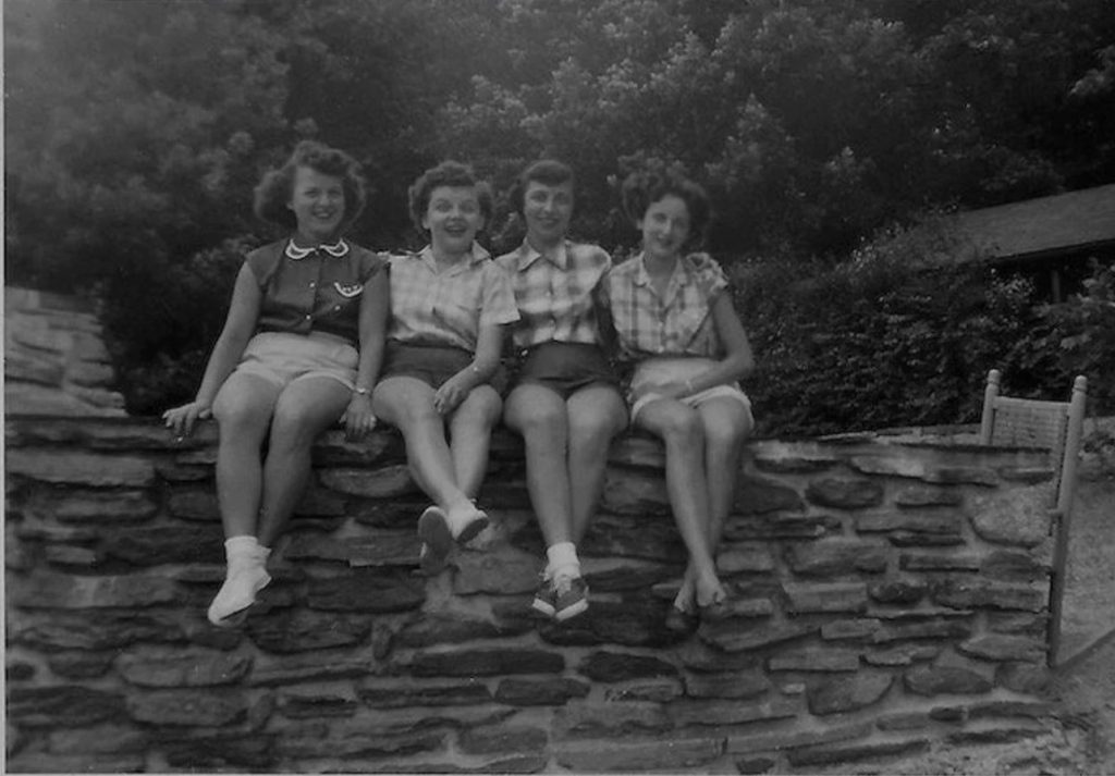 1950s vintage photo of 4 young women in shorts sitting on a wall in 1950s summer fashions