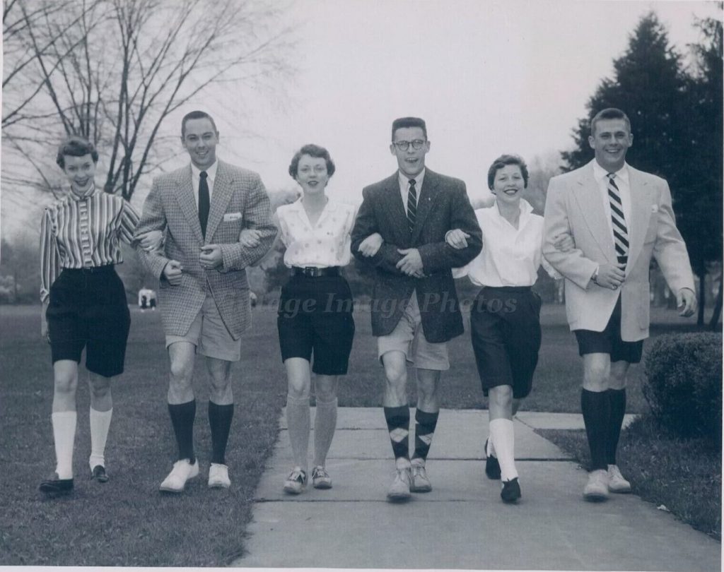 1950s vintage photo of men and women in 1950s fashions all wearing shorts including the men who are also wearing suit jackets with their shorts. 