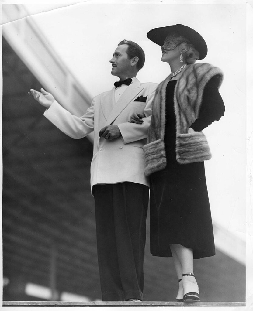 1940s vintage photo from Toronto's Canadian National Exhibition featuring a stylish couple in 1940s fashions/ The man is in a tuxedo and the woman is wearing a fur jacket, black dress and a hat with a veil. 