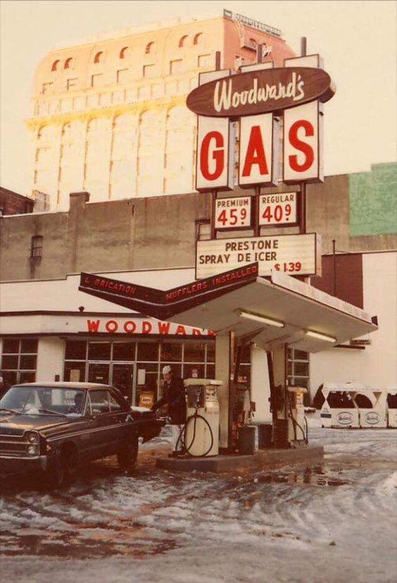 1960s vintage photo of a 1960s Gas Station at Woodward's Department Store. Image showcases a man pumping gas at the pump. 