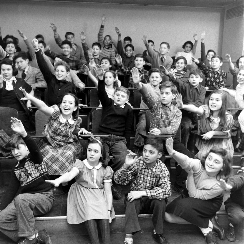 1940s vintage photo of kids raising their hand at a School For Kid Geniuses, 1948. LIFE visited what might be called a genius school at Hunter College—a school filled 450 apparently well-adjusted, engaged kids from ages three to 11, who just happened to enjoy IQs averaging around 150.