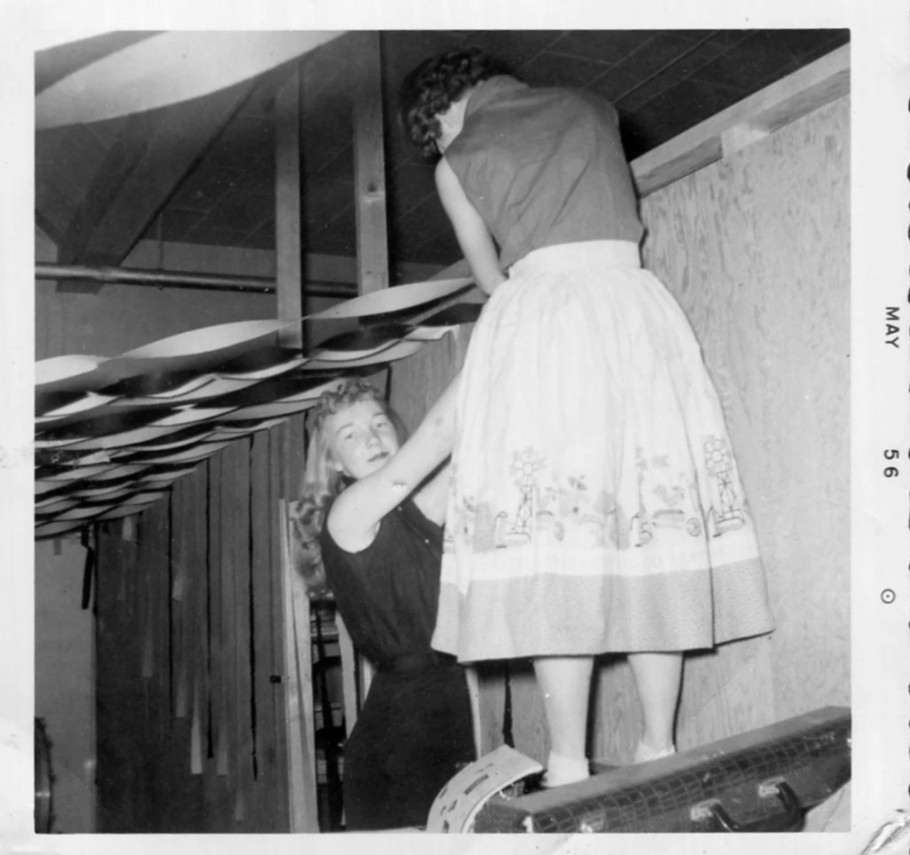 1950s vintage photo (May 1956) of 2 teenage girls in 1950s fashions decorating their gym for a school dance. Super 1950s skirt on the woman in the front of the image. 