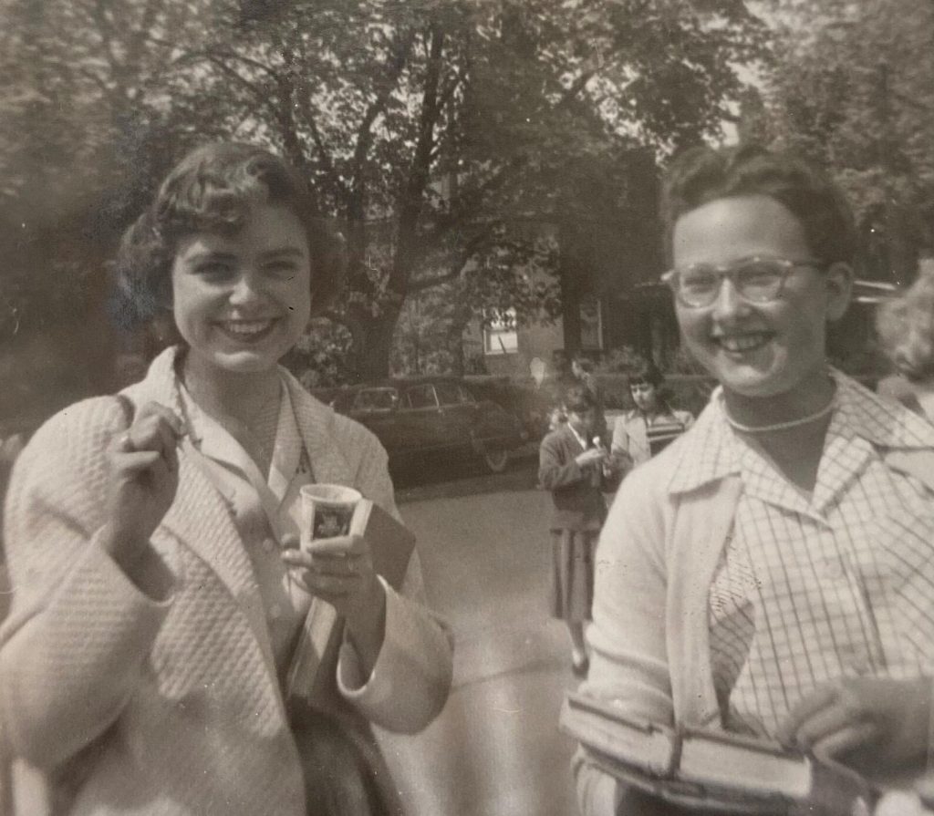 1950s vintage photo of two teenage girls in 1950s cardigans and blouses and 1950s hairstyles enjoying an ice cream while holding their books. 