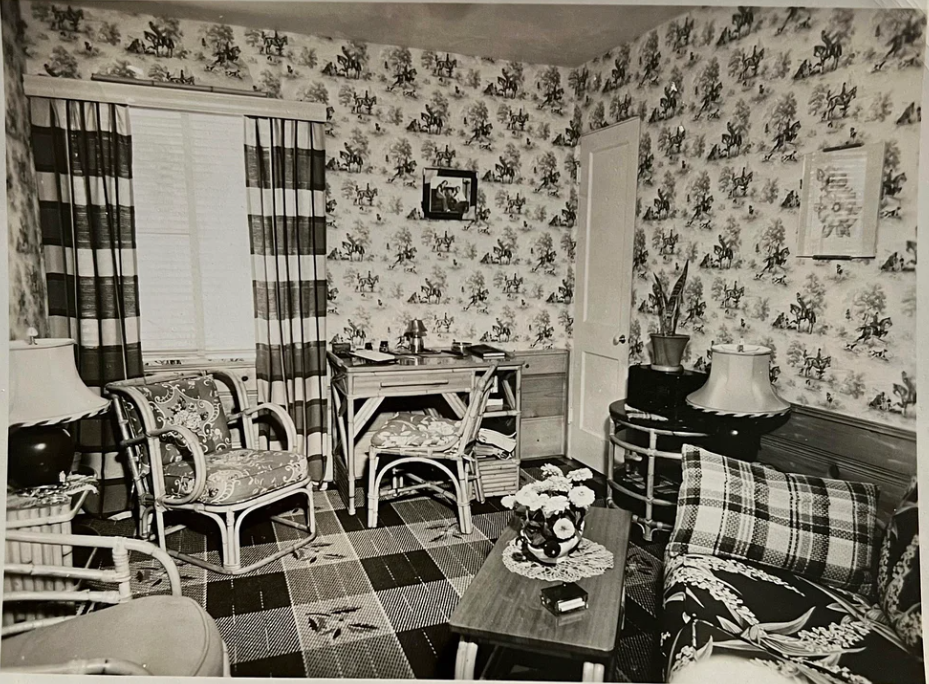 1950s vintage photo of a mid century living room filled with lots of interesting interior design choices. Plaid curtains, horse wallpaper, Rattan furniture and floral cushions. 