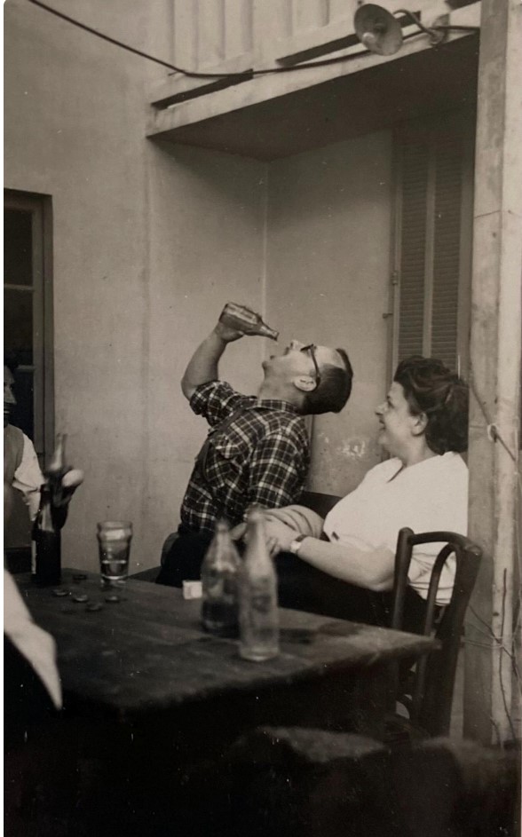 1950s vintage photo of a man in a plaid shirt downing a beer at a table