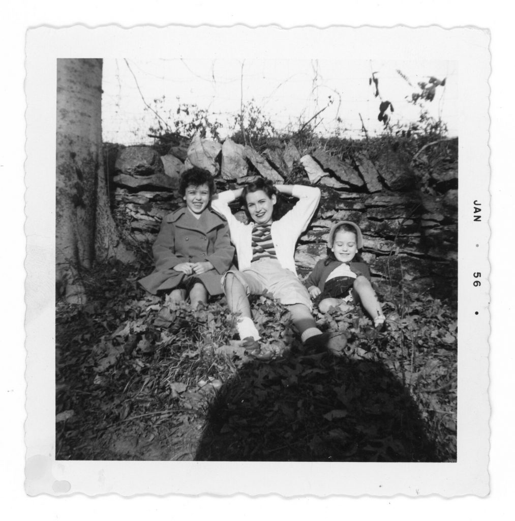 1950s Vintage Photo from January 1956 of a mother and her two kids posing a pile of leaves in their 1950s fashions. Our mom is wearing a cardigan over her shirt. Must be mild out! 