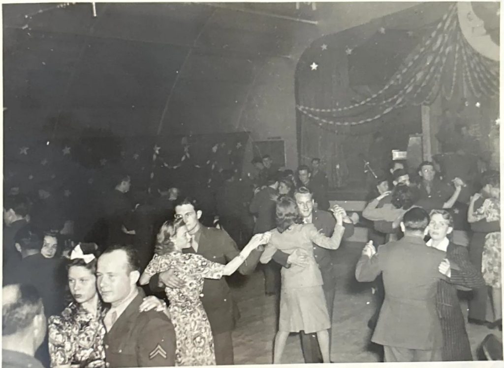 1940s vintage photo of a WW2 dance featuring soldiers dancing with women in 1940s fashions and 1940s hairstyles. 