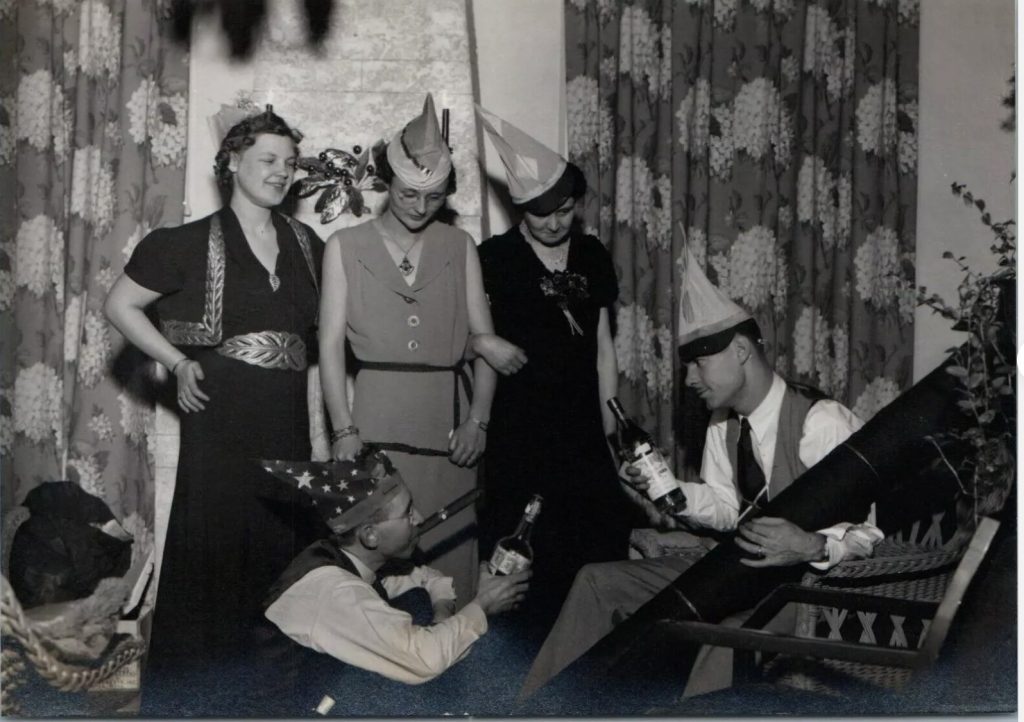 1930s vintage photo featuring women and men in 1930s fashions celebrating New Year's Eve while wearing party hats. 