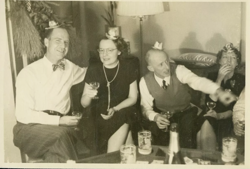 1940s 1950s vintage New Years Eve photo featuring couples wearing party hats drinking together on a couch