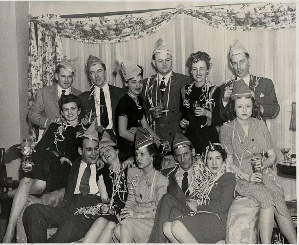 1940s vintage photo fo a group of men and women in 1940s fashions posing together in NYE Party hats on New Years Eve