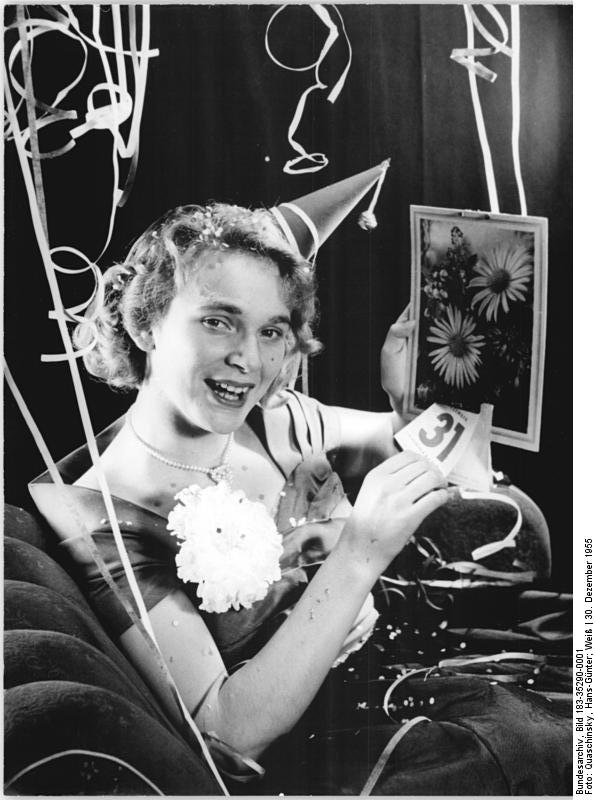 1950s vintage photo of a woman wearing a New Years eve party hat turning over the calendar in a 1950s evening gown