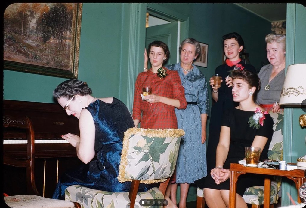 1950s vintage photo: Vintage Christmas photo of women at a festive party playing the piano in 1950s fashions and Christmas corsages. 