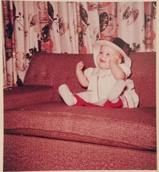 1960s vintage photo of a baby in a New Years Eve party hat sitting on a couch. - 1961 Photo. 